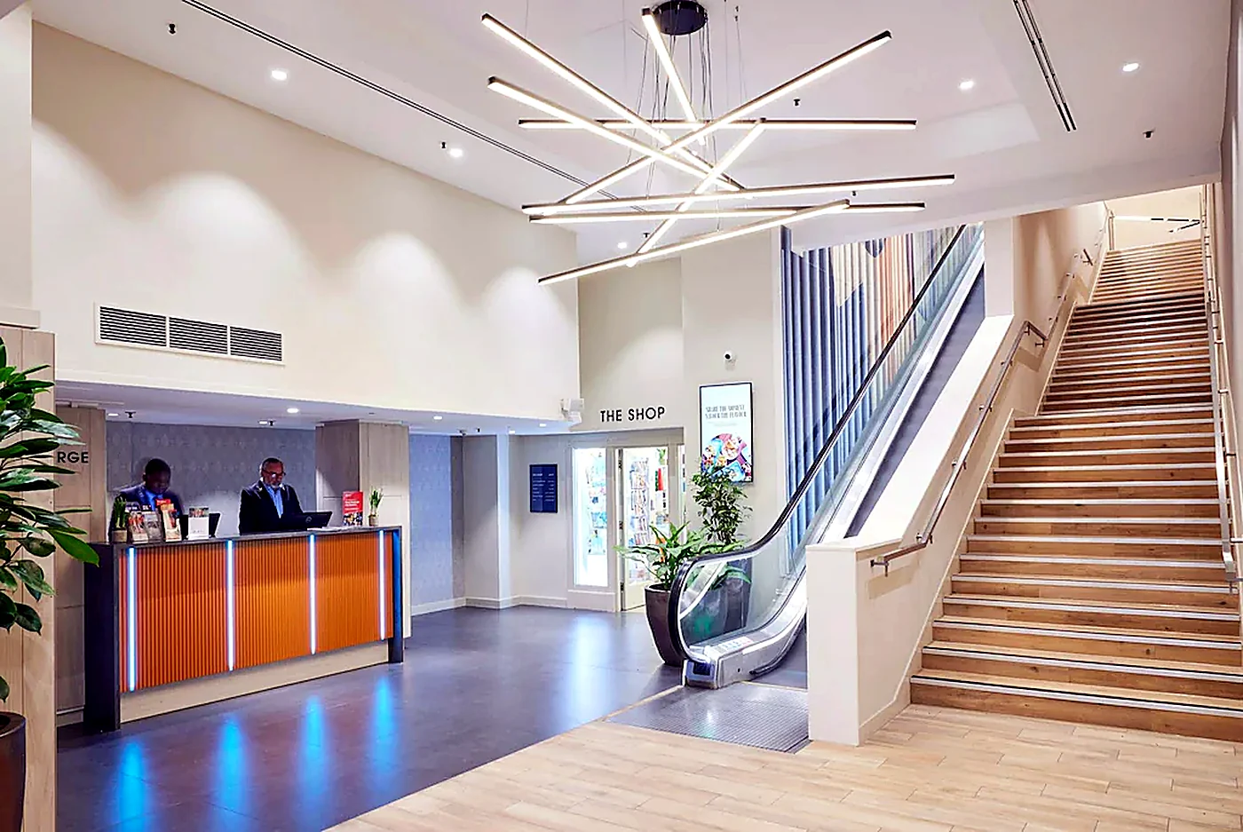 Hotel lobby with reception desk, escalator and statement ceiling lights