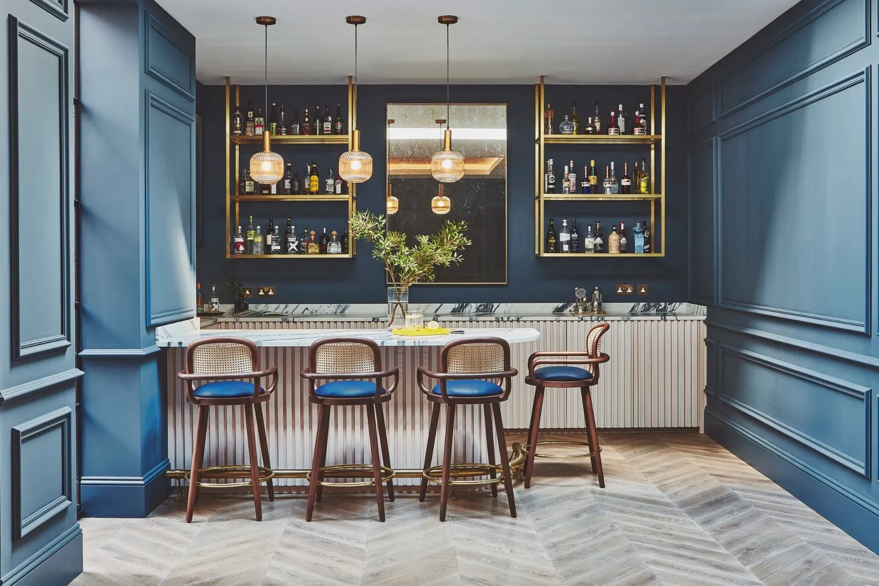 Bespoke home bar with dark blue wall panelling, brass shelving and marble worktop